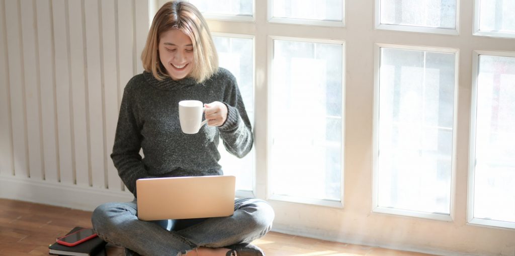 young woman having coffee while looking at her laptop