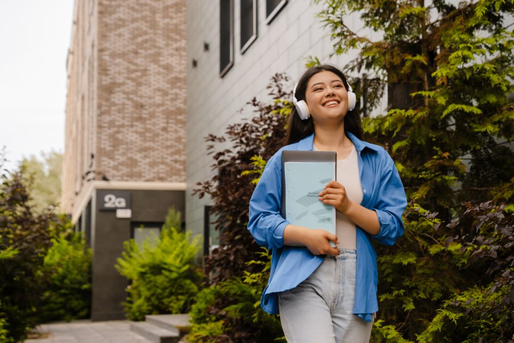 a female student wearing a headphone and holding her laptop