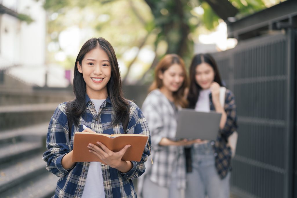 a student holding a note book with her friends behind her back