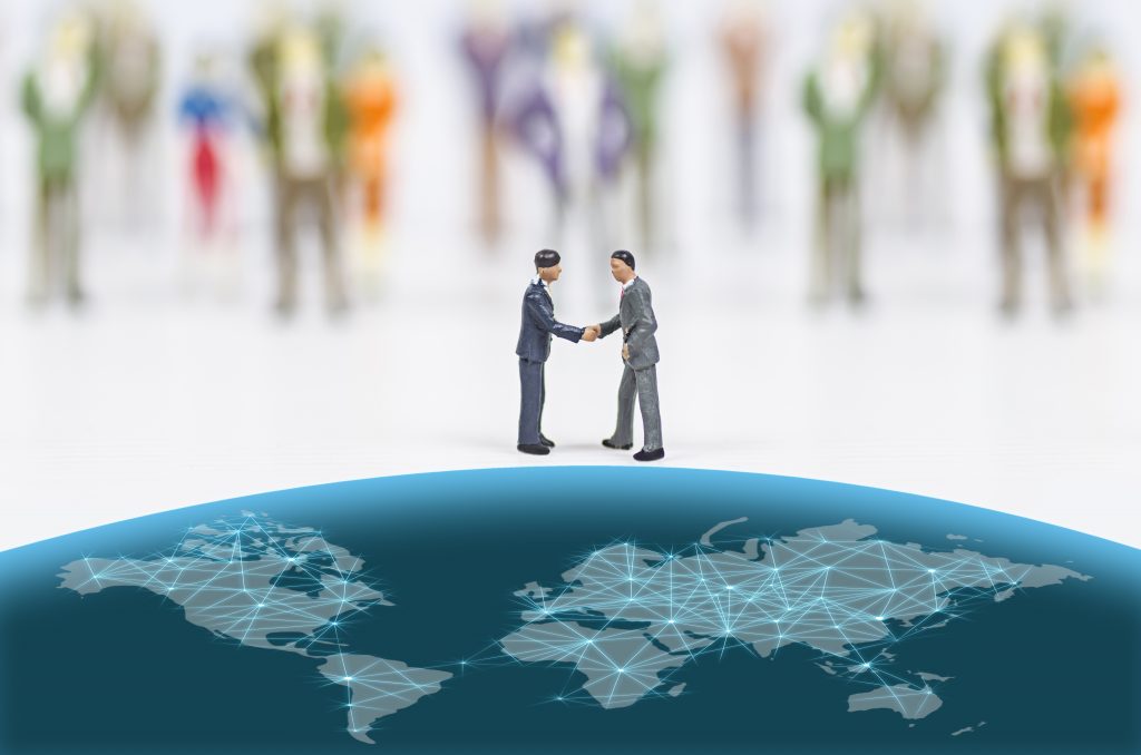 two miniature people shaking hands on top of a globe