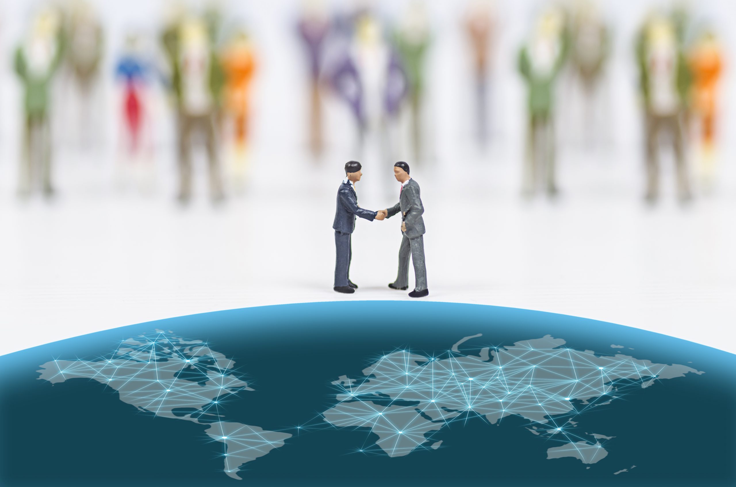 two miniature people shaking hands on top of a globe