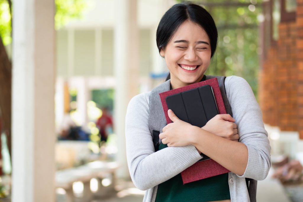 a woman holding her books and tablet smiling