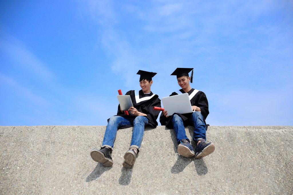 two graduating students sitting on a hand rail