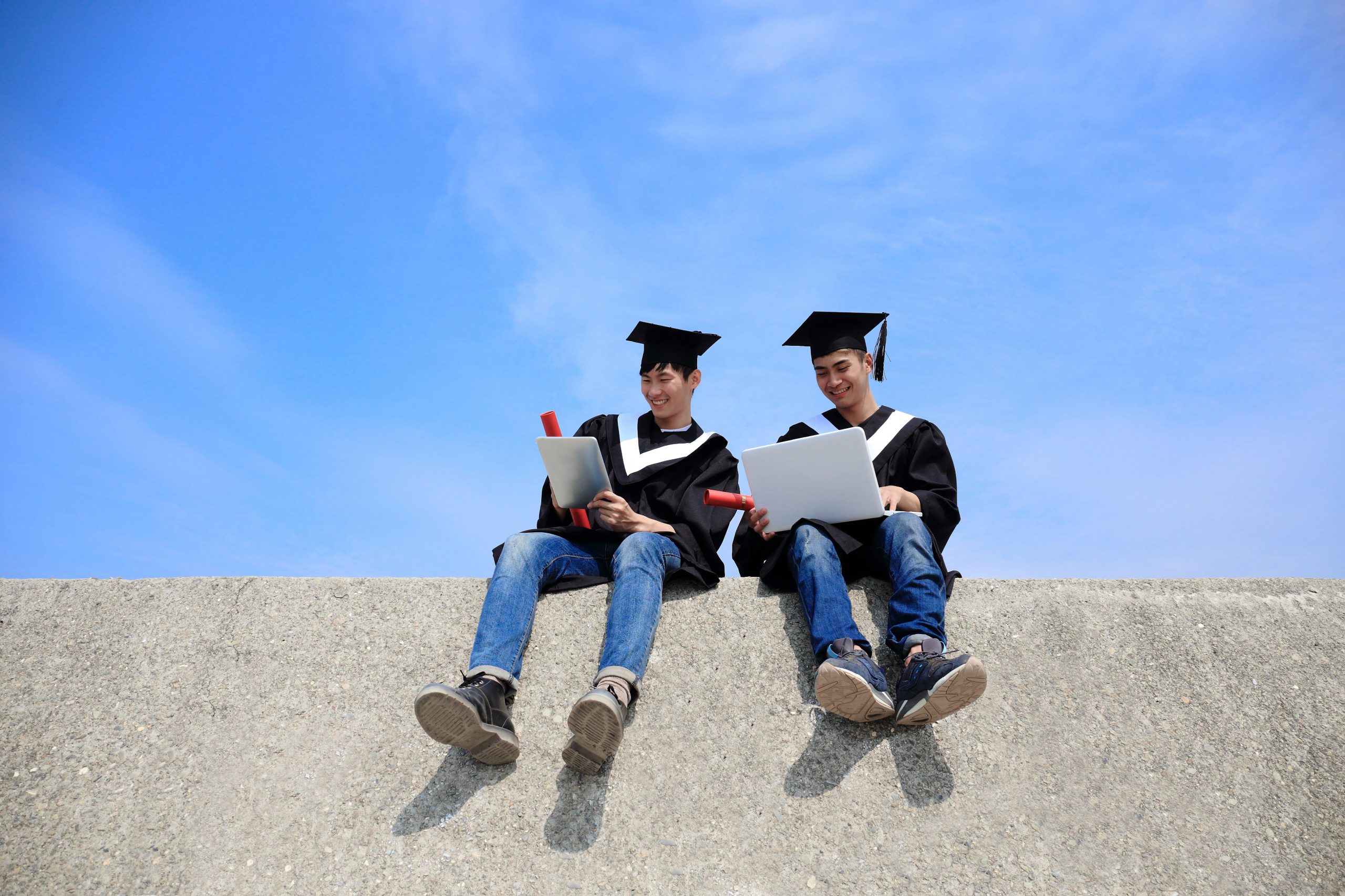 two graduating students sitting on a hand rail