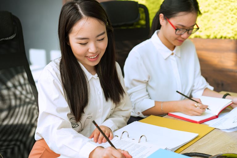 Two young professionals working together in a bright environment, taking notes and collaborating on a project.