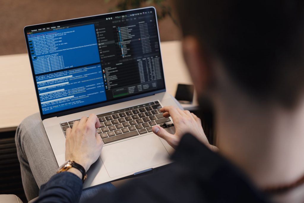 Man in a dark sweater working on a laptop with command-line interface visible