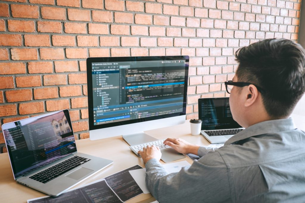 Software developer at a desk with three screens showing code and a coffee cup nearby