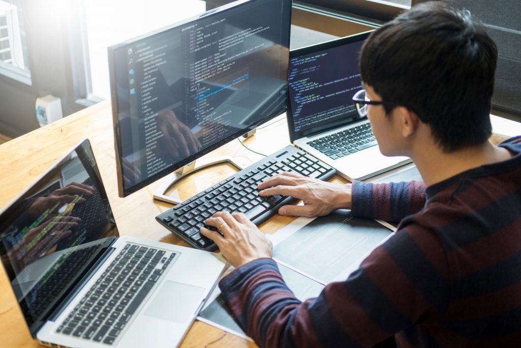 A student typing on a keyboard surrounded by multiple monitors displaying code
